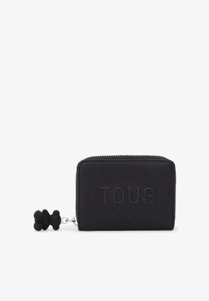 Cartera de cuero negro texturizado con el logotipo "TOUS" en relieve, cierre de cremallera y un charm en forma de oso negro adjunto. Diseño compacto y rectangular.