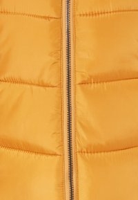 Gul puffervest med en skinnende, glat tekstur. Har en frontlynlås med sort hardware og vandrette quiltede sektioner.