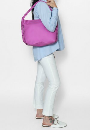 Borsa a spalla rosa con tracolle intrecciate, texture liscia, design spazioso, indossata con camicia azzurro chiaro e pantaloni bianchi.