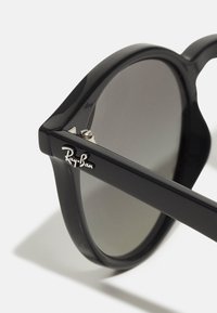 Mustad mustad Ray-Ban prillid ümmarguste läätsedega, millel on läikiv viimistlus. Tempel on varustatud eredad hõbedast detailid, mis kannavad kaubamärgi logo.