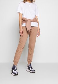 Camiseta blanca de Nike, pantalones de chándal beige y zapatillas tipo chunky multicolor. Sudadera atada a la cintura. Tejido suave, ajuste casual.
