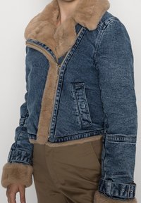 Chaqueta de mezclilla con un cuello y puños de pelaje sintético en marrón claro, diseño corto, cierre con cremallera y bolsillos laterales, con una textura de lavado azul.