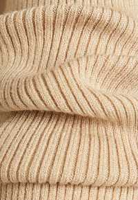 Tessuto di maglione a coste beige, morbido al tatto con strisce spesse e sottili alternate, finitura liscia, piegato per mostrare profondità e dettagli.