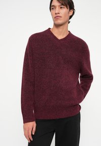 Burgundia soonik, millel on V-kaelus ning ribakujulised mansetid ja alumine äär, pehme tekstuuri ja lõdva lõikega.