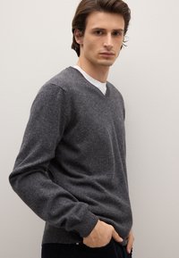 Schwarze Wolle V-Ausschnitt Pullover in Anthrazit, mit langen Ärmeln und gerippten Bündchen, getragen über einem weißen Rundhalsshirt.