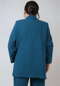 Teal blazer with a straight cut, notched lapels, and long sleeves. Smooth fabric with a tailored fit, featuring a central back seam.
