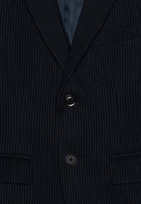 Niebieski żakiet w paski z wyłogowym kołnierzem, dwoma przednimi kieszeniami, pojedynczym zapięciem na guzik i gładką podszewką. Teksturowana tkanina z detalami.