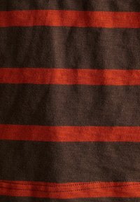 Nahaufnahme eines Stoffes mit horizontalen roten und dunkelbraunen Streifen, der die Stricktextur und leichte Falten zeigt.