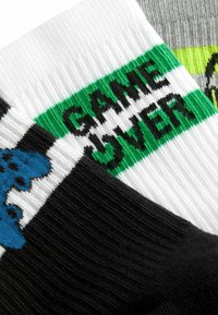 Pamut zoknik fekete alappal, fehér és szürke csíkokkal, valamint egy zöld szalaggal, amelyen vastag fekete betűkkel szerepel a "GAME OVER" felirat.
