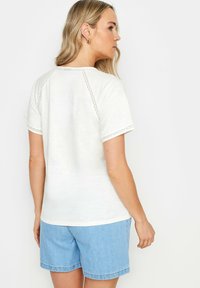 Top bianco a maniche corte con un design testurizzato sulle spalle, abbinato a pantaloni corti in denim azzurro chiaro. Tessuto morbido e vestibilità rilassata.