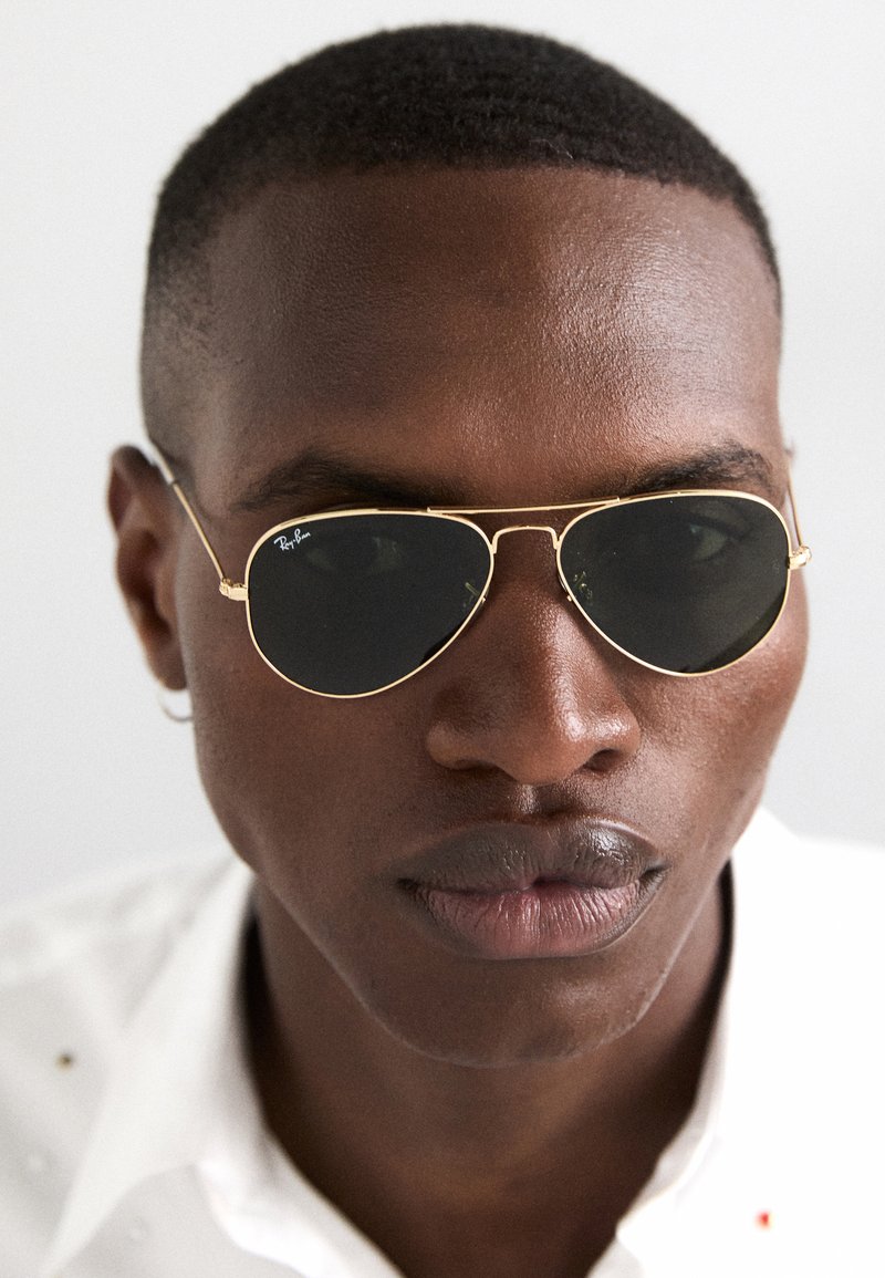 Ray-Ban aviator sunglasses with a gold metal frame and black lenses. The design features a double bridge and thin side arms.
