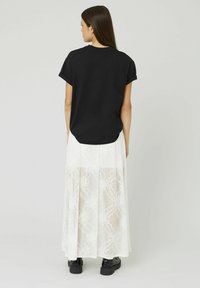 Haut noir à manches courtes associé à une longue jupe blanche en dentelle présentant des motifs complexes et une texture semi-transparente. Des chaussures noires complètent le look.