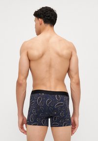 Blaue gemusterte Boxershorts mit einem schwarzen Bund, die ein Paisleymuster in Weiß- und Grautönen zeigen. Glatte Stofftextur.