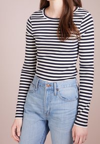 Marineblå och gräddfärgad randig långärmad tröja med rund halsringning, kombinerad med högmidjade ljusblå denimjeans.