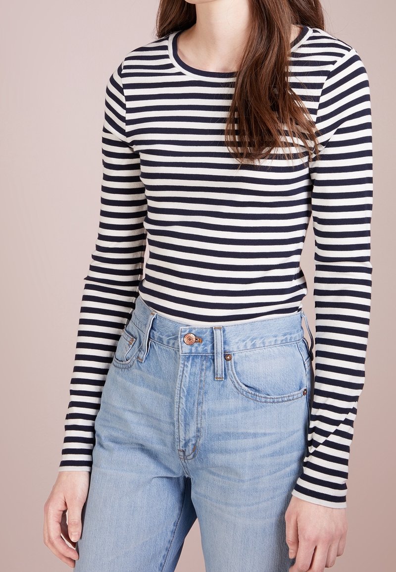 Marineblå och gräddfärgad randig långärmad tröja med rund halsringning, kombinerad med högmidjade ljusblå denimjeans.