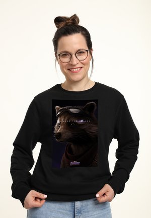 Sort sweatshirt med et grafisk motiv af en vaskebjørn med solbriller, sat mod en mørk baggrund, med teksten "HÆVN DE FALNE."