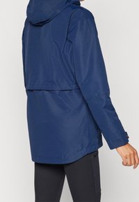 Navy blue, mid-length jacket with a hood, made of smooth, water-resistant fabric. Features a cinched waist and long sleeves.