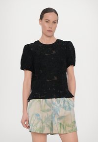 Zwart, gestructureerd T-shirt met korte mouwen en een bloemenkantpatroon in een rechte snit, gecombineerd met lichte pastel shorts met een palmbladprint.