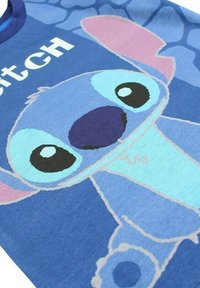 T-shirt en coton bleu avec un personnage de dessin animé aux grands yeux et oreilles, imprimé dans des nuances de bleu, rose et violet. Comprend le texte "Stitch".