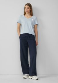 Bluza w paski o jasnoniebieskim kolorze z dekoltem w serek, połączona z szerokimi spodniami w ciemnym odcieniu granatu. Stylizacja charakteryzuje się swobodnym krojem i luźnym fasonem.
