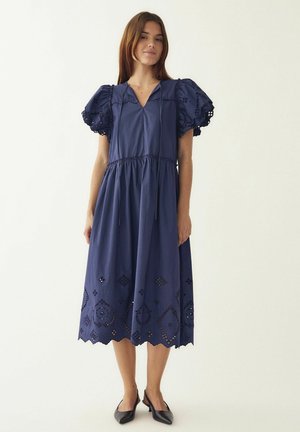 Tmavomodré bavlnené šaty s nadýchanými rukávmi, výstrihom do V a vyrezávanými vzormi pri leme so škvrnitými okrajmi.