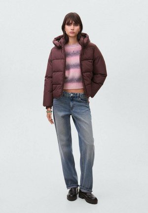 Chaqueta marrón acolchada con capucha, diseño corto, llevada sobre un suéter de punto a rayas en rosa y gris, combinada con jeans rectos de color azul claro y botas negras.
