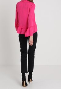 Blusa rosa a maniche lunghe con orlo a campana. Abbinata a jeans neri a vita alta e tacchi a stiletto neri. Tessuto dalla superficie liscia.