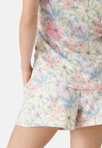 Lounge-set med blommönster i pastellrosa, blå och gula blommor på en krämfärgad bakgrund. Mjukt tyg, ledig passform med fickor.