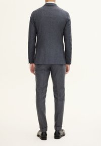 Completo grigio su misura realizzato in tessuto testurizzato, caratterizzato da un giubbotto monopetto con revers a lancia e pantaloni slim-fit con risvolti.