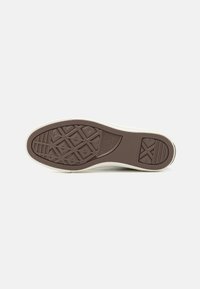 Suela de zapatilla de goma marrón con patrones texturizados, ribete blanco y logotipo distintivo. El diseño presenta ranuras para tracción.