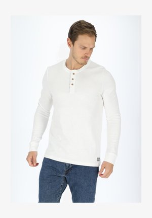 White long-sleeve henley shirt made of ribbed fabric, featuring a round neckline, three-button placket, and a logo tag at the bottom.