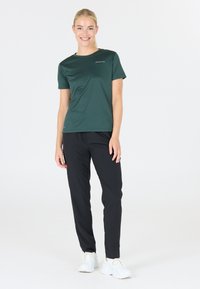 Grön atletisk t-shirt med slim fit och korta ärmar, i kombination med svarta tapered byxor och vita sneakers, med synlig logotypdetalj på t-shirten.