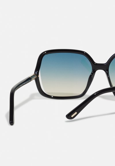 Occhiali da sole neri oversize con lenti a gradiente che passano da blu scuro a chiaro nella parte inferiore. Presentano una forma squadrata arrotondata e aste eleganti.