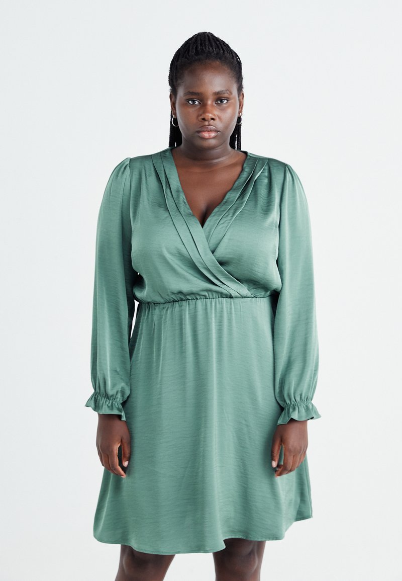 Vihreä kietaisumekko kevyestä kankaasta, jossa on pitkät puff-hihat ja kerätty vyötärö, joka on sileä tekstuuriltaan ja V-päällyksellä.