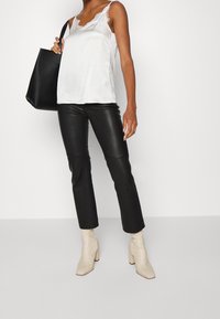 Camisola de satén blanco con encaje, combinada con pantalones de imitación de cuero negro de campana y botines de tacón ancho crema. Bolsa tote negra.