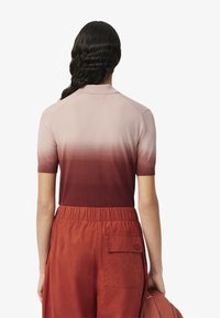 Polo à manches courtes avec un dégradé ombragé allant du rose clair au rouge foncé. Fabriqué en tissu doux, il présente un col et des bords légèrement côtelés.