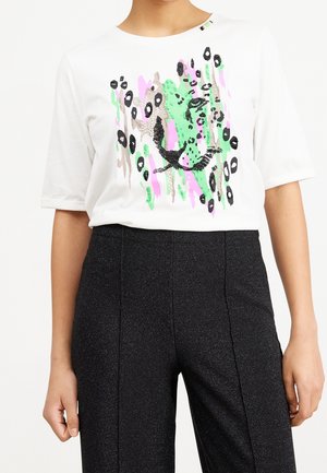 Haut blanc à manches courtes avec un motif abstrait de visage de léopard en noir, vert, rose et beige, associé à un pantalon noir texturé taille haute.