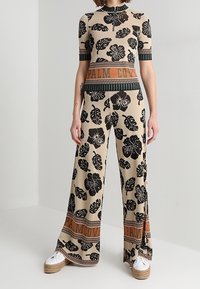 Conjunto de dos piezas de punto en beige con un patrón de hojas negras. Incluye una blusa de manga corta y pantalones de pierna ancha, con un detalle de una franja naranja.