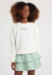 Sudadera blanca con el texto "EL FIN DEL VERANO" en verde, combinada con una falda de cuadros verde menta en capas. Tejido texturizado y ajuste suave.