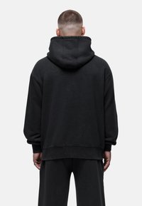 Felpa nera oversize con cappuccio foderato, polsini a coste e dettagli di cucitura sottili. Tessuto liscio con una finitura opaca.