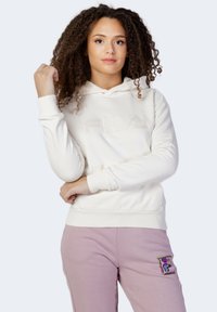 Felpa bianca in pile con tasca a marsupio frontale e logo embossato. Abbinata a pantaloni sportivi rosa pastello con una colorata toppa con logo.