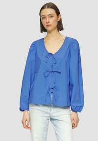 Blaue Langarmbluse mit tiefem V-Ausschnitt und drei Vorderbändern, ausgestattet mit Puffärmeln und aus einem glatten, leichten Stoff.