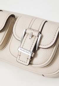 Lys beige pebble-lærveske med sølvdetaljer, med en frontklaff og spenne, akkompagnert av sydd kanter.