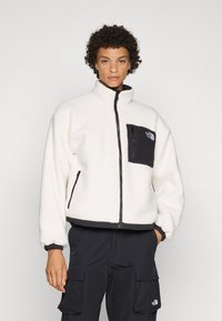 Mikina zo fleece v off-white farbe s čiernymi akcentmi, vysoký golier, zipsové zapínanie a vrecko na hrudi. Mäkká textúra s elastickými manžetami.