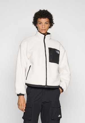 Fleecejakke i off-white med svarte detaljer, høy krage, glidelåslukking og brystlomme. Myk tekstur med elastiske mansjetter.