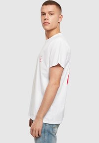 Hvid bomulds t-shirt med korte ærmer, der har et pink logo på venstre bryst. Pasform er almindelig og suppleres med lyseblå denim jeans.