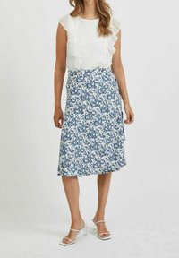 Bílá volánková blůza v kombinaci s modro-bílou květinovou sukní. Sukně má design do zavinování a vzdušnou texturu. Bílé páskové podpatky.