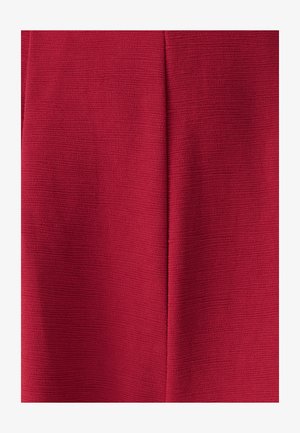 Roter strukturierten Stoff mit einer kräusligen Oberfläche, der eine zentrale vertikale Naht aufweist. Das Material scheint gewebt zu sein und hat eine weiche, taktile Qualität.