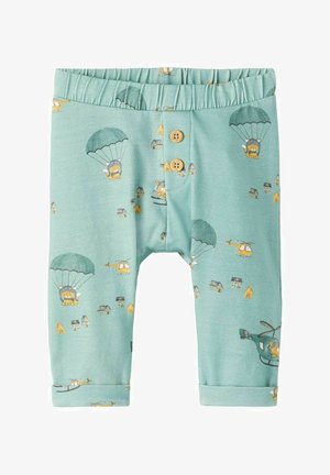 Pantalones de bebé color verde agua claro con cintura elástica, dos botones de madera y estampados de leones haciendo paracaidismo, helicópteros y casitas pequeñas.