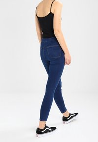 Jeans ajustados de denim azul oscuro, con una cintura alta y un diseño clásico de cinco bolsillos, combinados con zapatillas Vans negras.